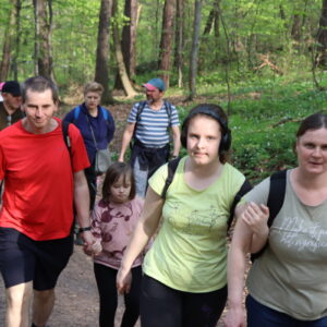 Zdjęcie przedstawia grupę osób idących ścieżką w lesie.