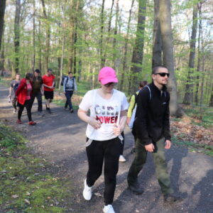 Zdjęcie przedstawia grupę osób idących szutrową ścieżką w lesie.