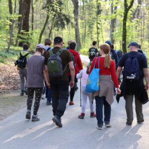 Zdjęcie przedstawia grupę osób idących asfaltową ścieżką w lesie.